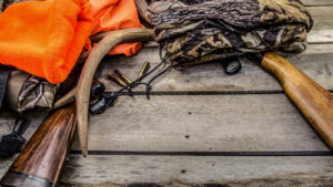 hunting rifles, deer antlers and hunting apparel laying on a wood table.
